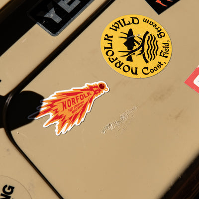 A close-up of a beige yeti with two Norfolk-themed stickers: a round yellow sticker reading 'Norfolk Wild Stream Coast, Field' and a red-orange flame-shaped sticker reading 'Norfolk'.